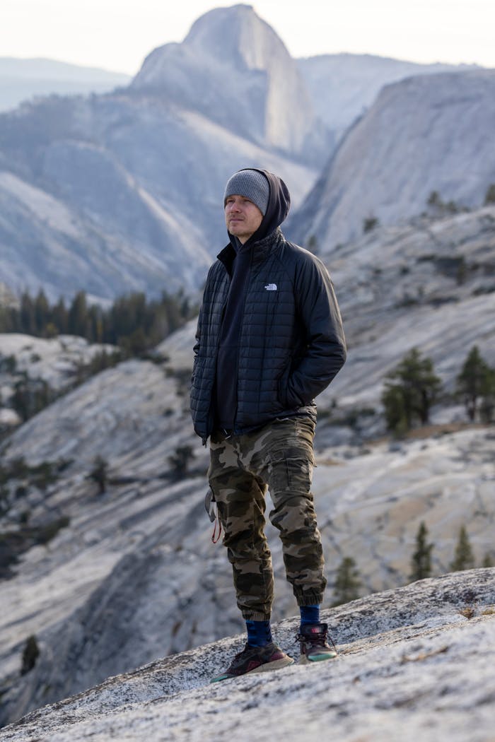A man stands on a rocky trail in Yosemite with Half Dome in the background.
